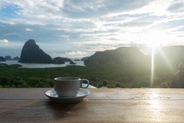 A cup of coffee on the table on wood table in the morning sunrise of Samet Nang She is the best and famous view point on Phang nga bay in Southern Thailand. - 355905767