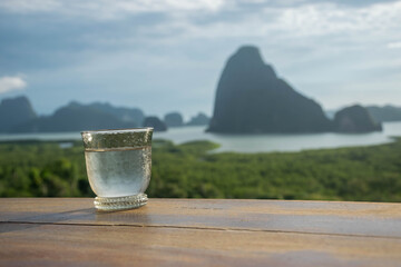Close up of water glass on wood table in the morning sunrise of Samet Nang She is the best and famous view point on Phang nga bay in Southern Thailand. - 355905793