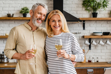 Happy middle aged couple drinking wine and looking in camera