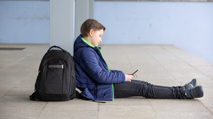 Truancy concept, young boy staying away from the school and playing games on the mobile, martphone,...