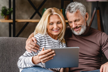 Smiling middle aged couple using digital tablet on sofa at home