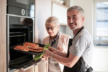 senior couple taking hot pastries out of the oven.