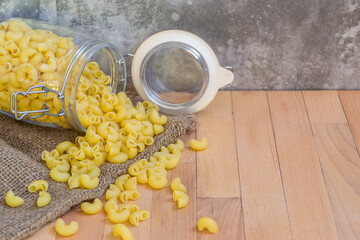 Close-up of Uncooked Macaroni in a glass jar placed on the wood table with Sack  , selective focus. - 355907588
