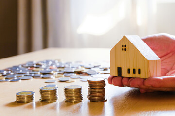 Men hand hold, giving wood house beside increasing money, coin stack on wood table. Saving plan to buy property, house. Personal financial concept for own a house. 