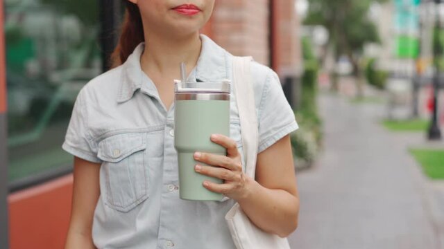 Young asian woman holding a reusable tumbler glass and walking in the city, Zero waste concept