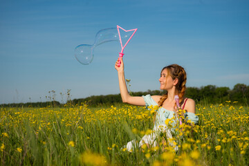 Happy beautiful girl on dress sitting i and relaxing on summer field.Cheerful beautiful woman  blows soap bubbles on sunny summer day on sunshine field. Summer holidays concept or summer sale.