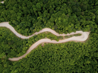 Mountain winding zig zag gravel road. Top aerial view: cars driving on road from above.