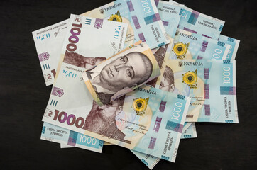 Obraz na płótnie Canvas rolled into a roll 500 hryvnia lie on banknotes of 1000 hryvnia. Black background. Financial concept.