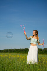 Happy beautiful girl on white dress walking and relaxing on summer holidays.Cheerful beautiful woman  blows soap bubbles on sunny summer day on sunshine field. Summer holidays concept or summer sale.
