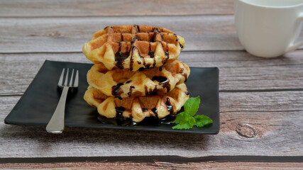 Homemade waffles with chocolate sauce in black plate on wooden table.