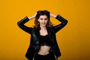 Excited young slim brunette female raising emotionally her hands while rejoicing about something, standing over yellow background in black sporty wear