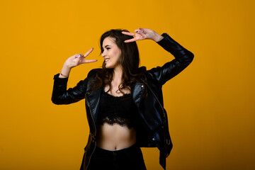 Excited young slim brunette female raising emotionally her hands while rejoicing about something, standing over yellow background in black sporty wear