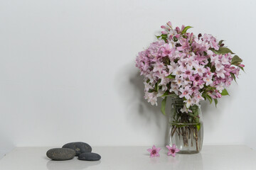 Interior decoration, pink rhododendron bouquet in glass vase, three black stones, copy space