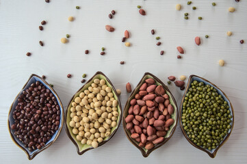 Various beans in ceramic bowl in a row, colorful beans scattered on white table