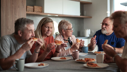 Mature friends sitting at the table in the home kitchen.