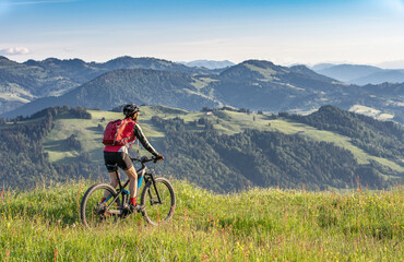 pretty senior woman riding her electric mountain bike on the mountains above Oberstaufen, Allgau Alps, Bavaria Germany 
