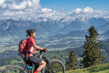 Fototapeta premium pretty senior woman riding her electric mountain bike on the mountains above the Iller valley between Sonthofen and Oberstdorf, Allgau Alps, Bavaria Germany 