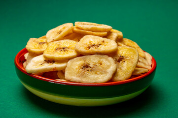 Healthy snack, crispy dehydrated unsugared banana chips in bowl on green background