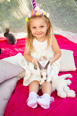 Cute little girl on nature in a unicorn hoop with rabbits.