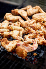 Man using metal tongs to turning chicken wings which are being grilled on barbecue, outdoor, meat is fried in mangal barbecue grill, Chef cooking in backyard at home.