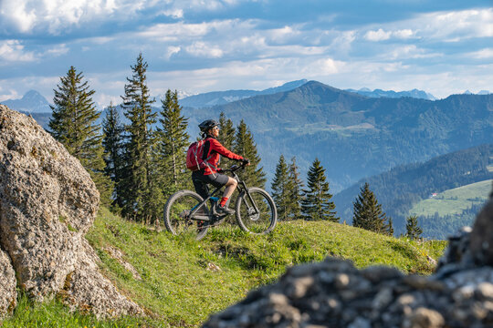 pretty senior woman riding her electric mountain bike in warm dawn sunlight and enjoying the spectacular view over the Allgau alps near Oberstdorf, Bavaria, Germany
