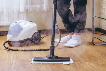 The woman washes the floor in the room with a white steam cleaner, a wet high-pressure steam....