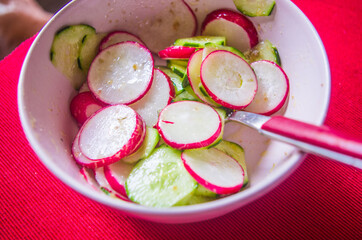 Radish and zucchini salad, with oil, salt and pepper on scarlet red tablecloth