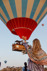 Beautiful blonde woman greets flying hot air balloon at dawn in Cappadocia