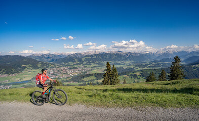 pretty senior woman riding her electric mountain bike on the mountains above the Iller valley between Sonthofen and Oberstdorf, Allgau Alps, Bavaria Germany
