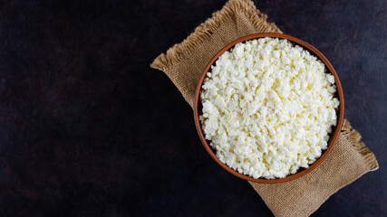 Cottage cheese on a burlap. Fresh cottage cheese on a dark background. Soft cheese on a black background. Minimalism. Top view. Copy space