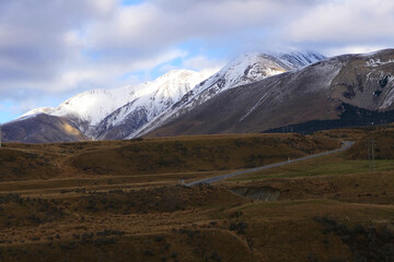 Road through the slightly snow covered Southern Alps in Canterbury New Zealand in the morning with clouds in the sky
