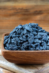 Black Raisins in the bowl on wooden rustic background 