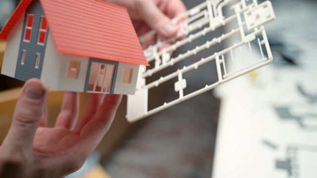 Male engineer using plastic and paper designer items for construction of masion model, property mockup for customers. Real estate construction project, living house in miniature. Engineering and