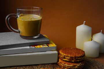 coffee mug, waffles, books and candles on a brown background