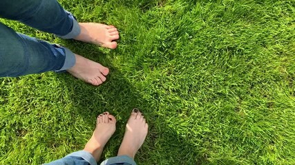 The bare feet of girls in jeans are dancing happily on the green grass POV. Concept of freedom and happiness. Feet with pedicure. Loop boomerang animation for instagram story. Vertical Video
