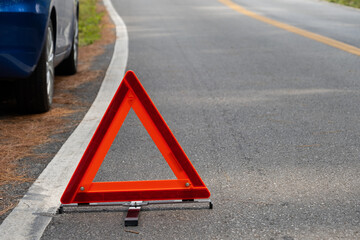Emergency red warning triangle on the road sign with the white road line and broken car