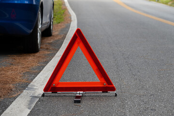 Emergency red warning triangle on the road sign with the white road line and broken car