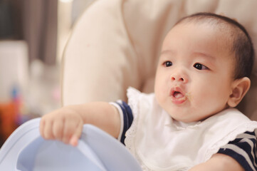 Asian baby boy sitting on a high chair, waiting for breakfast ,eating  first time at home