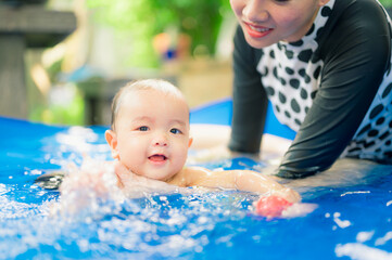 Fototapeta na wymiar Asian mother swimming with cute adorable baby in swimming pool, during quarantine,Fun holiday concept.