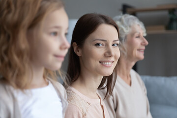 Close up profile view of three generations of women look in distance dreaming or visualizing, smiling young Caucasian mother look at camera, girl with mom and grandmother show family unity and bonding