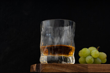 A glass of golden whiskey standing on wooden table together with white grape