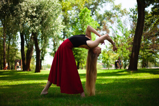 Photo of a young belly dancer in a park. A young blonde is dancing in nature. Girl gymnast in a red skirt.
