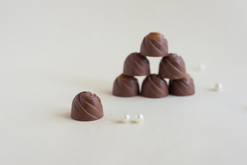 Chocolate candies stand in a pyramid and one in the foreground, on a light background. Soft focus