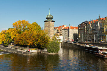 Fototapeta na wymiar Ancient tower on the river bank in the fall. Autumn Prague. Landscape.
