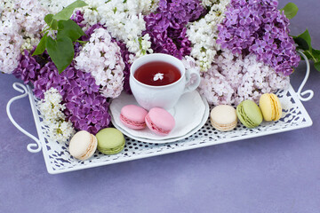 on a lilac table on an old white tray a cup of tea, macaroons and a bouquet of lilac