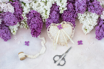 on a light background lace heart, ribbon, scissors and a bouquet of lilacs