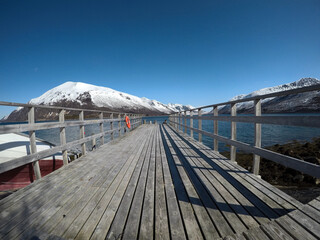 old pier going into the deep blue fjord with snowy mountain backdrop in northern norway