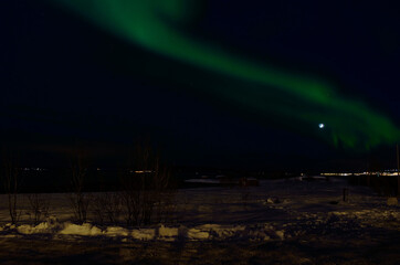 aurora borealis dancing over snowy field near sea shore with full moon