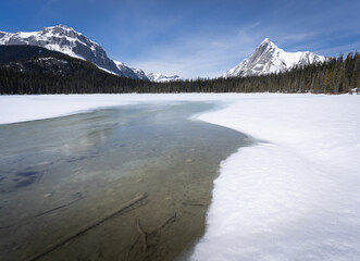 Half frozen alpine lake surrounded by snowy mountains, shot at Watridge Lake, Kananaskis, Alberta, Canada