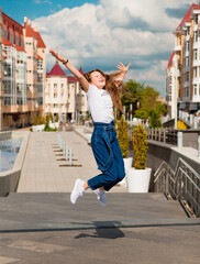 summer, leisure and people concept - happy little girl jumping high on city background. The area of...